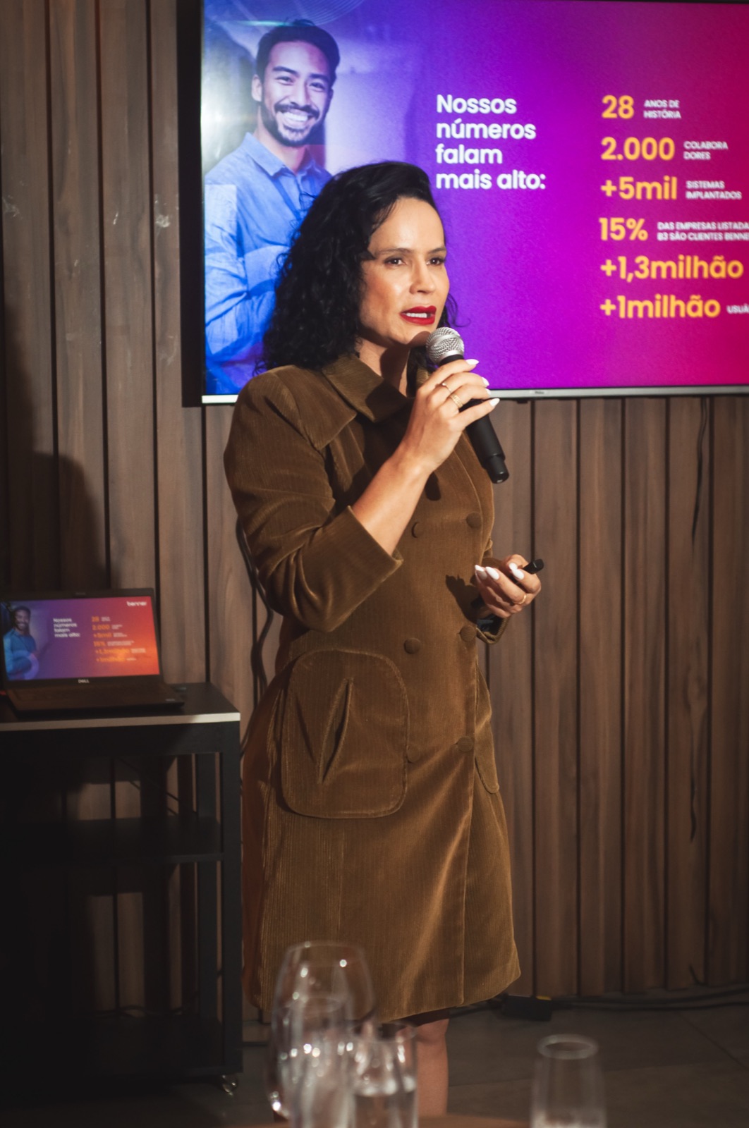 Palestrante ao microfone com apresentação no telão durante o evento da Benner