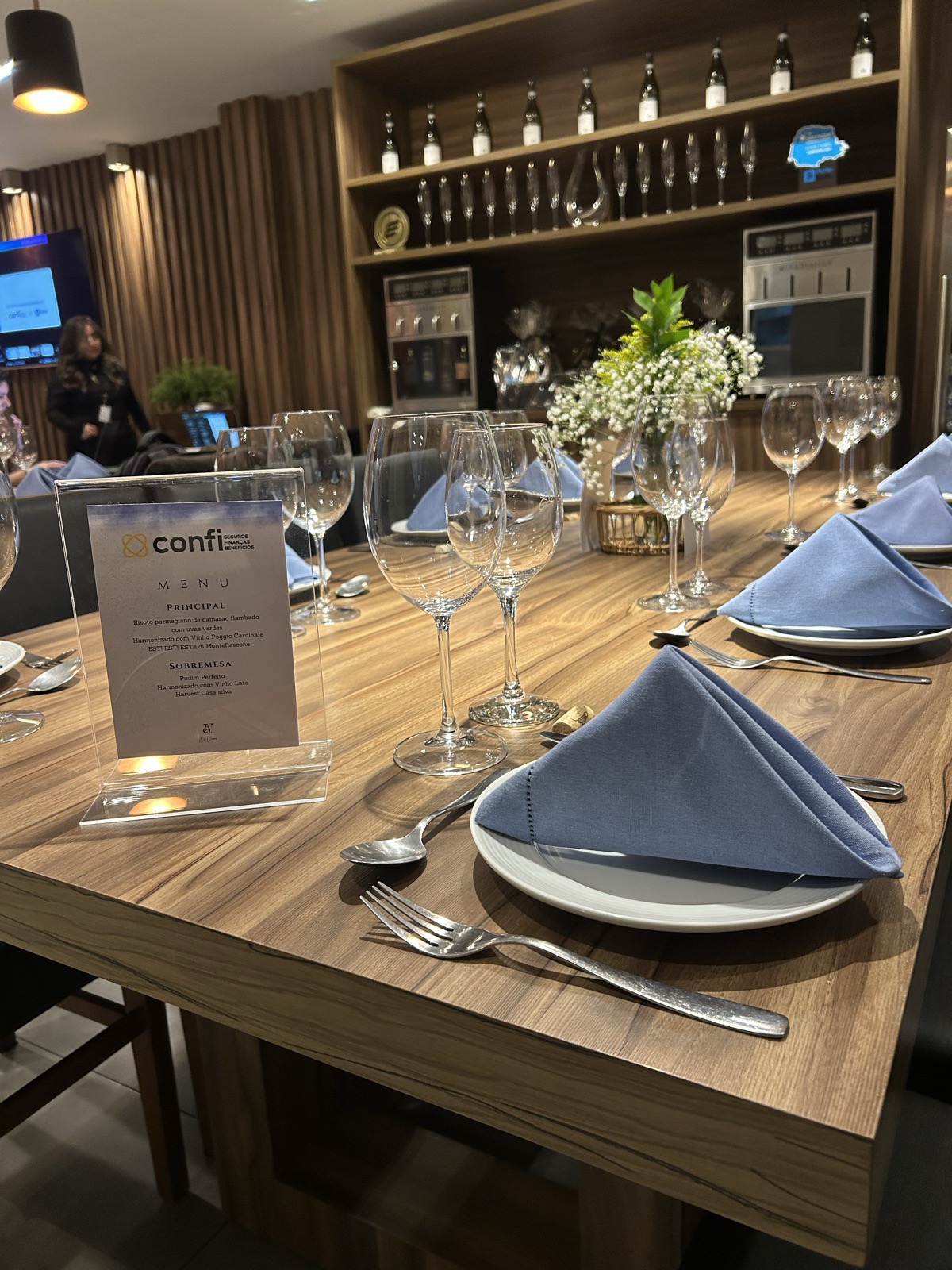 Menu personalizado da Confi Seguros sobre a mesa posta com taças e guardanapo azul