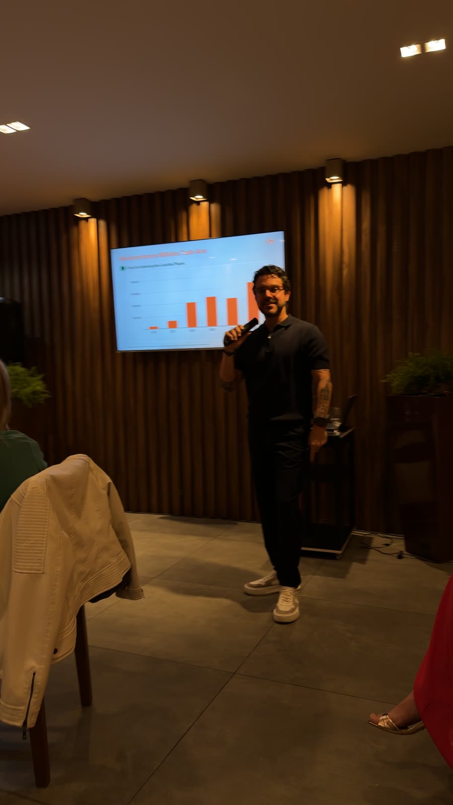 Apresentador ao microfone com gráficos de resultados no telão durante o Conexão Loft Curitiba