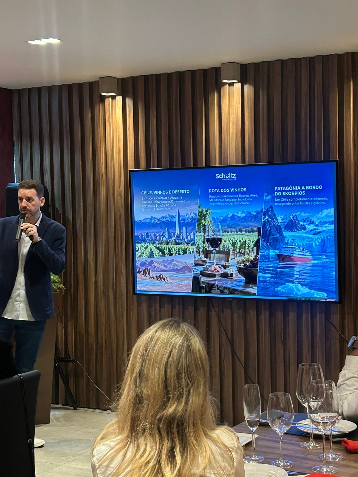 Apresentação da Schultz ao microfone, ao lado da tela e das mesas preparadas para o encontro com agências no El Vinos Gastrowine.